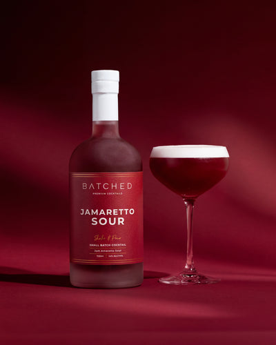 Batched Jamaretto Sour cocktail bottle and glass on a red background